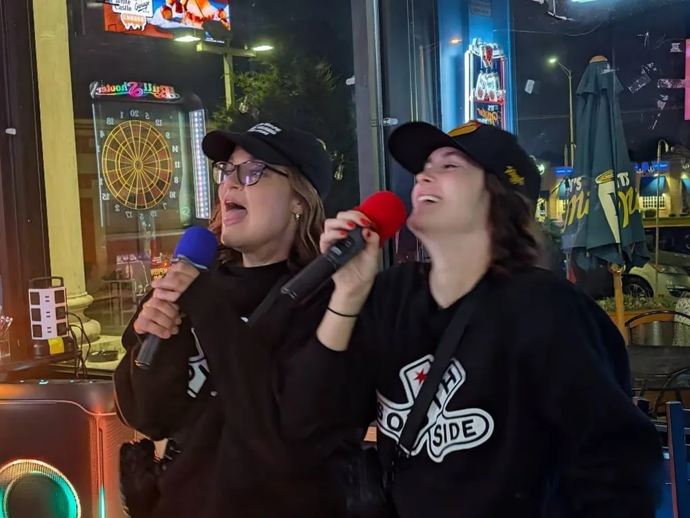 Two women singing into colorful microphones at Sam’s Bar and Gaming